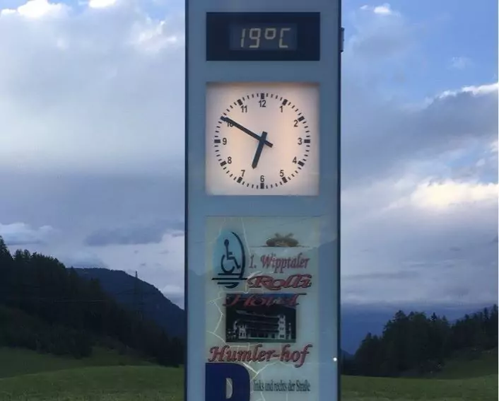 Eine Standuhr die kurz vor 19 Uhr zeigt - im Hintergrund Berge