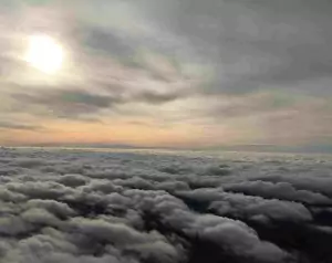 über den Wolken mit Sonne als Lichtfleck zwischen weiteren Wolken