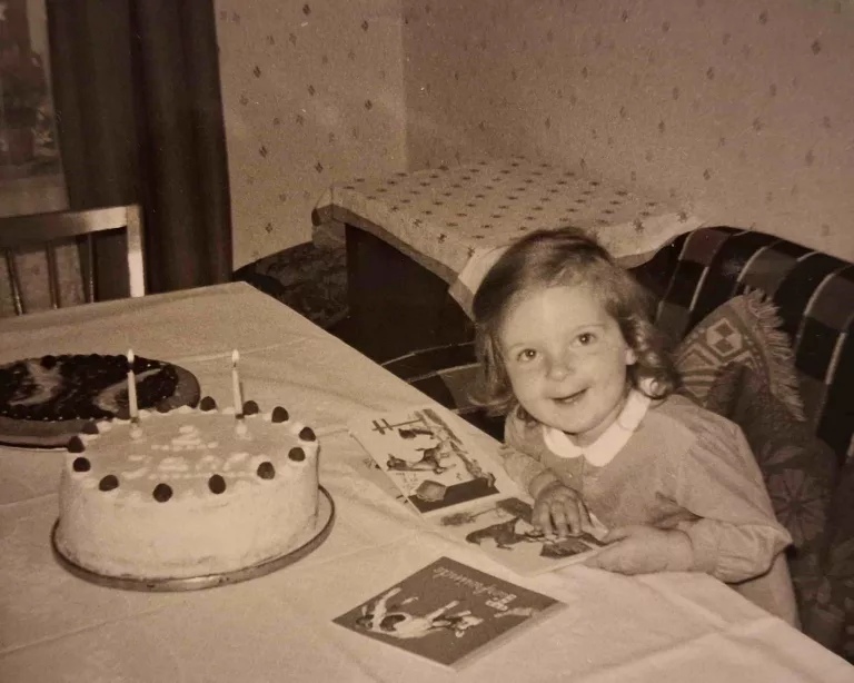 Kleines Mädchen sitzt auf dem Sofa vor einer Geburtstagstorte mit zwei Kerzen